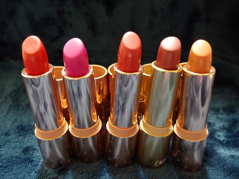 Five opened lipsticks with gold package components on a blue blanket.